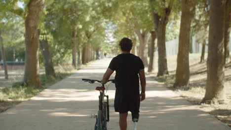 Back-view-of-man-with-bionic-leg-walking-down-alley-with-bike